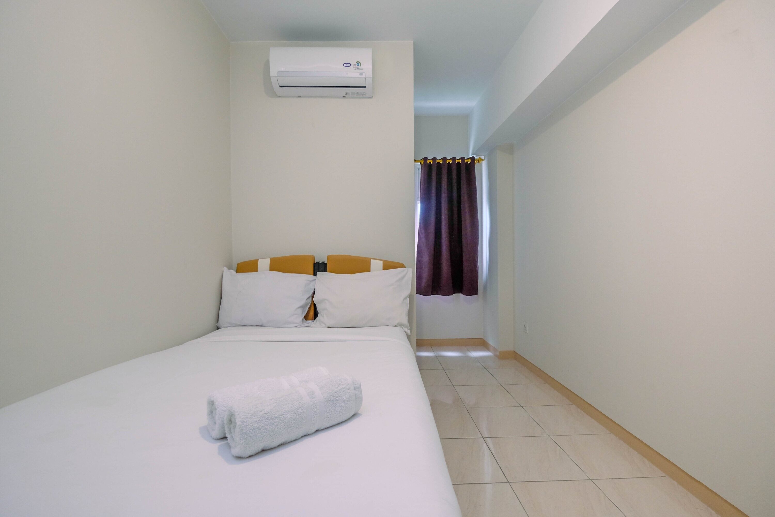 Una habitación pequeña y limpia con una cama individual, aire acondicionado de pared y una ventana con cortinas moradas.
