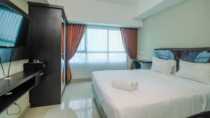 A hotel room with a bed, a TV, a desk, and a window with curtains.