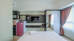 A hotel room with a bed, a television mounted on the wall, a minibar, and a sliding door to the bathroom.