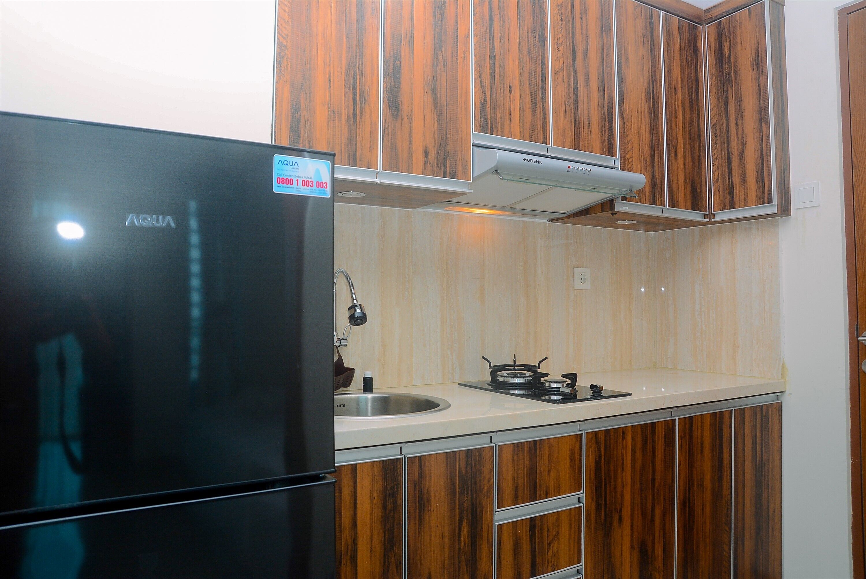 A kitchen with wooden cabinets, a black refrigerator, a gas stove, and a stainless steel sink.