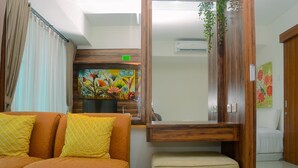 A living room with a sofa, ottoman, and a painting on the wall. - Cozy and Simple Living 1BR Grand Kamala Lagoon Apartment (Bekasi)
