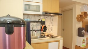 A compact kitchen with a stainless steel kettle, a stove, and a microwave. - Comfort and Nice 2BR at Meikarta Apartment (Cikarang)