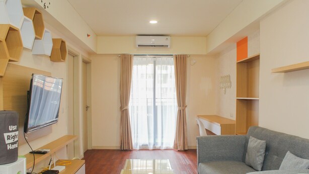A modern living room with a flat-screen TV, a glass-top coffee table, a grey sofa, and a wooden cabinet. - Comfort and Nice 2BR at Meikarta Apartment (Cikarang)