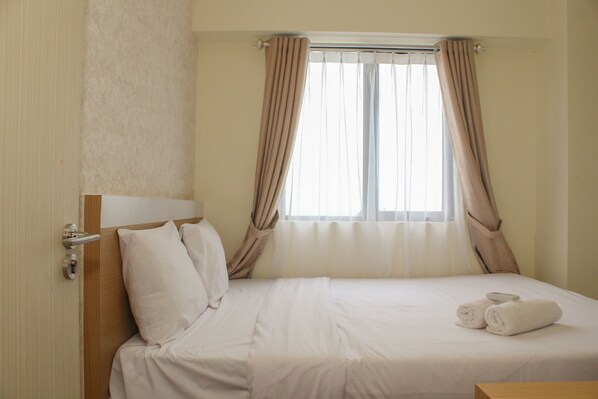 A hotel room with a bed, curtains, a window, and a door.
