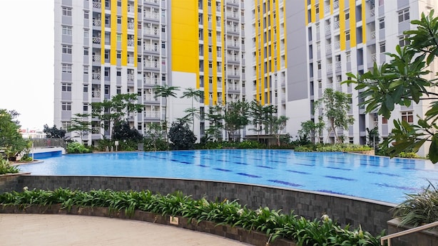 Piscina rodeada por vegetação, com um edifício alto ao fundo.