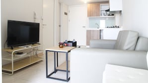 Uma sala de estar moderna com uma televisão de tela plana, uma mesa pequena e um sofá cinza.