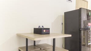 A compact kitchenette with a black refrigerator, a small table with two stools, and a box labeled 'Travelio' on the table. - Homey and Cozy Stay 2BR at Meikarta Apartment (Cikarang)