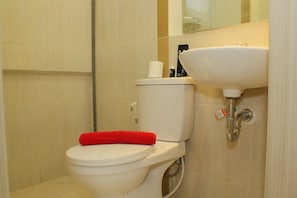 A bathroom with a toilet, a red towel on the seat, a white sink, and a mirror above the sink.