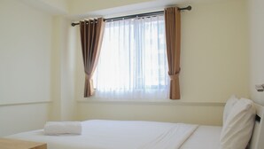 A hotel room with a bed, a wooden nightstand, and a window with curtains. - Cozy and Relax 2BR at Meikarta Apartment (Cikarang)