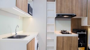 A compact kitchen with a built-in washing machine, a microwave, and a stove. - 2BR with Sofa Bed at Springlake Summarecon Apartment (Bekasi)