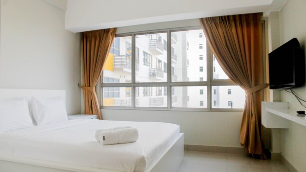 A hotel room with a large bed, a television on the wall, and a window with curtains. - Homey Studio at Springlake Summarecon Bekasi Apartment (Bekasi)