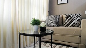 Una sala de estar con un sofá color crema, cojines estampados en blanco y negro, una pequeña mesa redonda con un florero blanco y un cuadro en la pared.