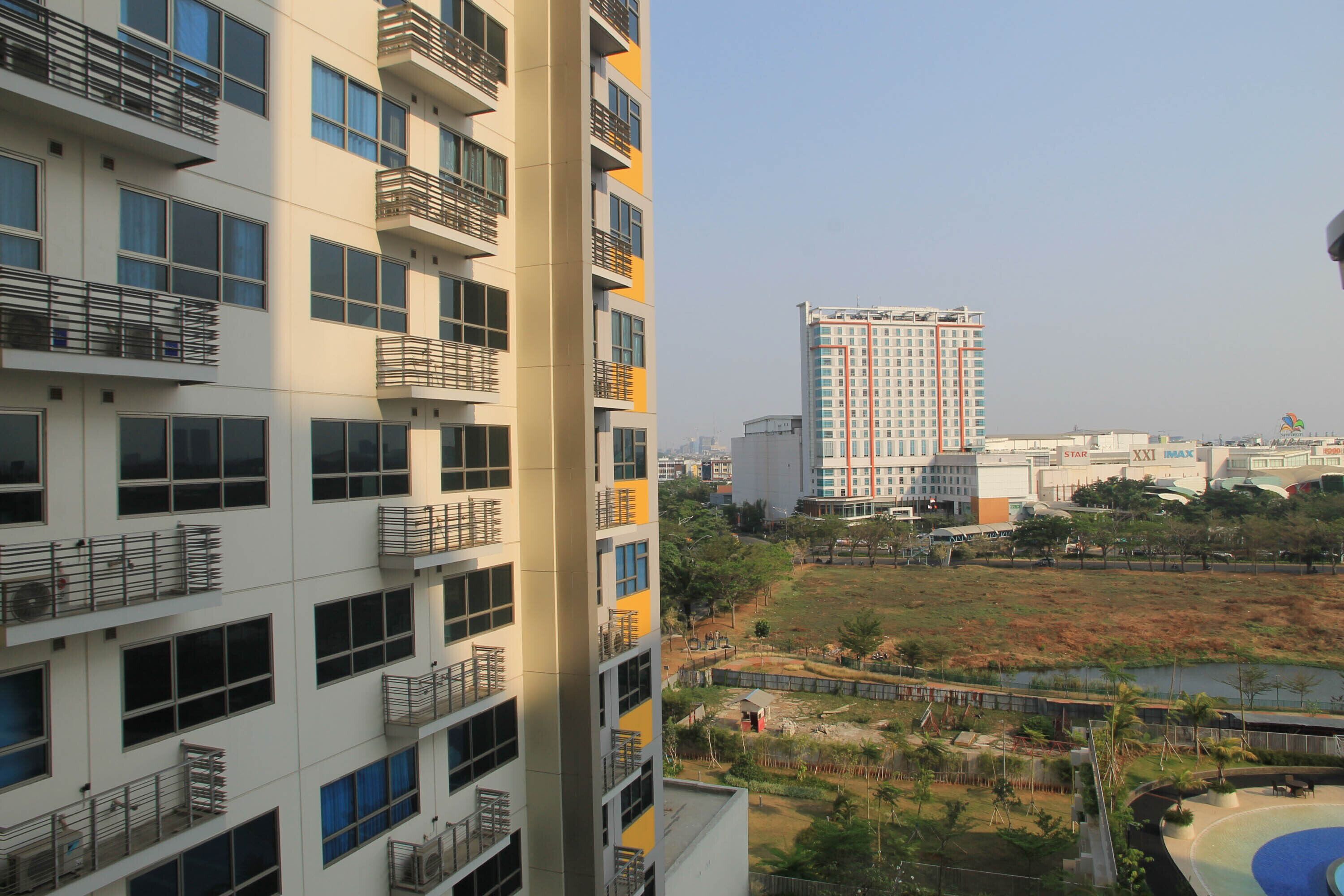 A multi-story residential building with balconies, a large open park area, and a distant high-rise building.