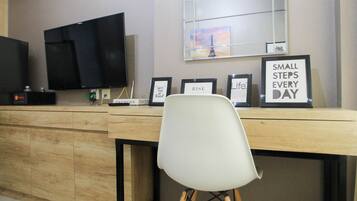 Een kamer met een houten bureau, een witte stoel, een flatscreen televisie en gemotiveerde citaten in lijsten aan de muur.