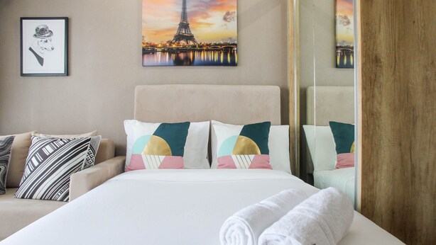 Habitación de hotel con cama, almohadas, un cuadro con la Torre Eiffel y un espejo que refleja la habitación.