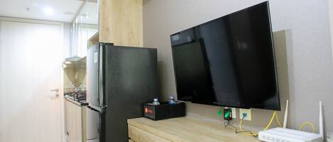 A compact kitchen with a refrigerator, a microwave, and a sink. A flat-screen TV is mounted on the wall, and a router is on the counter.
