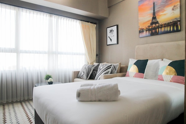A hotel room with a large bed, a view of the Eiffel Tower, a small table with a plant, and a sofa with patterned cushions.