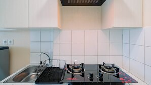A modern kitchen with a gas stove, a sink, and a black metal rack. - Wonderful Studio The Springlake Summarecon Apartment (Bekasi)