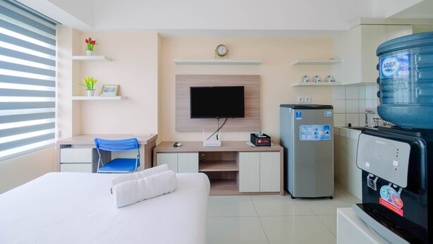 A hotel room with a bed, a desk with a chair, a television, a refrigerator, and a water dispenser. - Wonderful Studio The Springlake Summarecon Apartment (Bekasi)
