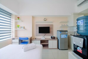 A hotel room with a bed, a desk with a chair, a television, a refrigerator, and a water dispenser. - Wonderful Studio The Springlake Summarecon Apartment (Bekasi)