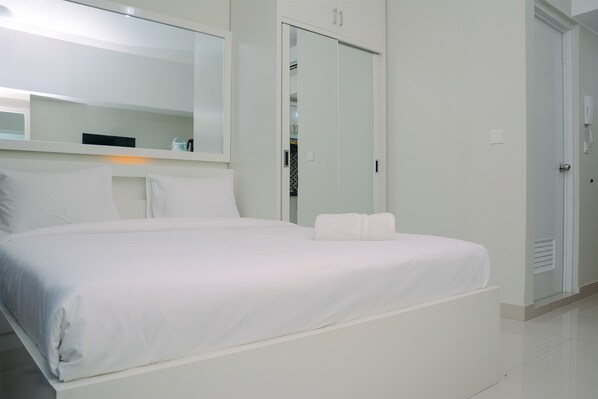 A modern hotel room with a large bed, a mirror, a wardrobe, and a door.