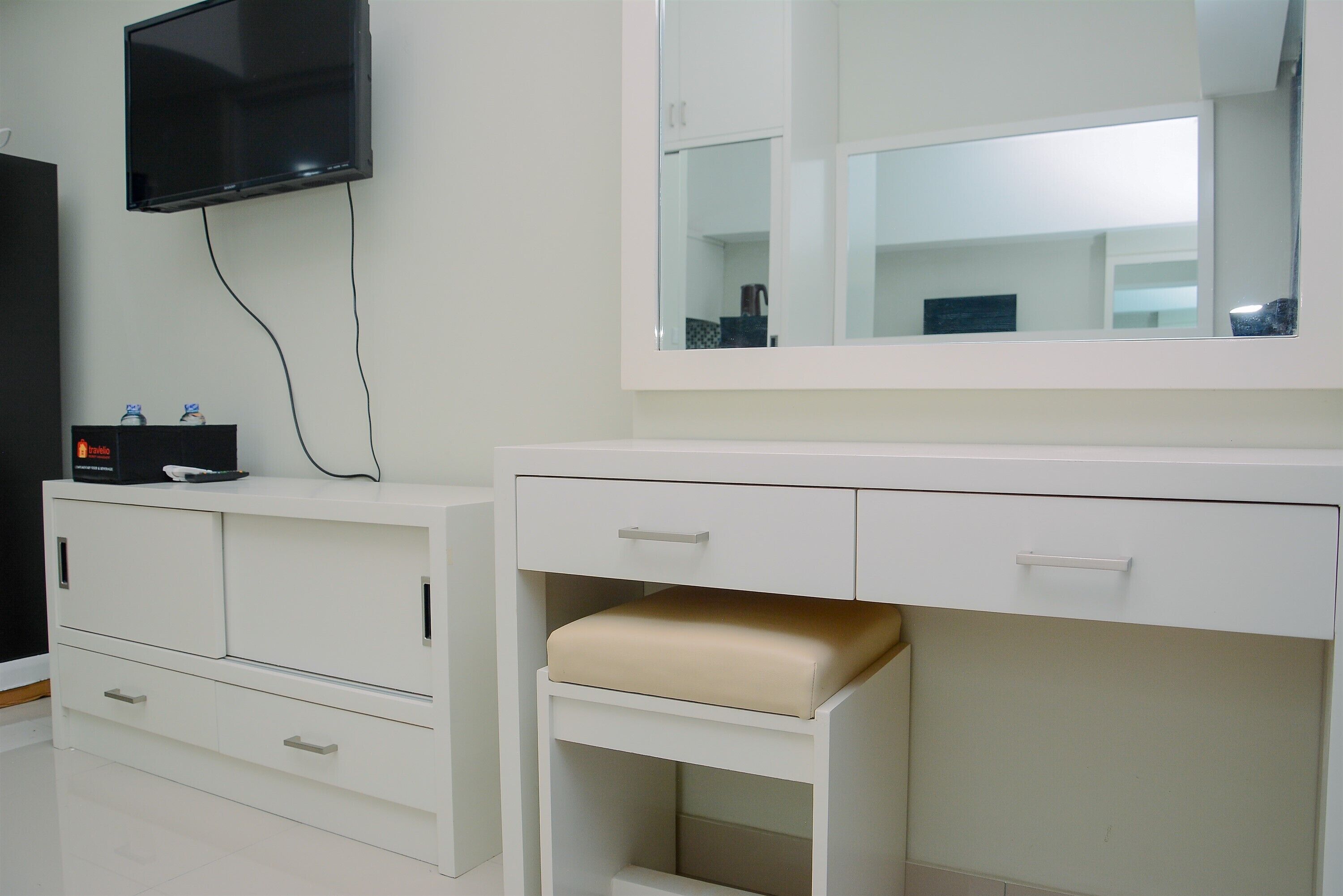 A modern bathroom with a large mirror, a television mounted on the wall, and a white vanity with drawers and a bench.