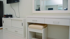A modern bathroom with a large mirror, a television mounted on the wall, and a white vanity with drawers and a bench. - Studio Apartment with Garden View at The Springlake View Summarecon (Bekasi)