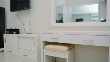 A modern bathroom with a large mirror, a television mounted on the wall, and a white vanity with drawers and a bench.