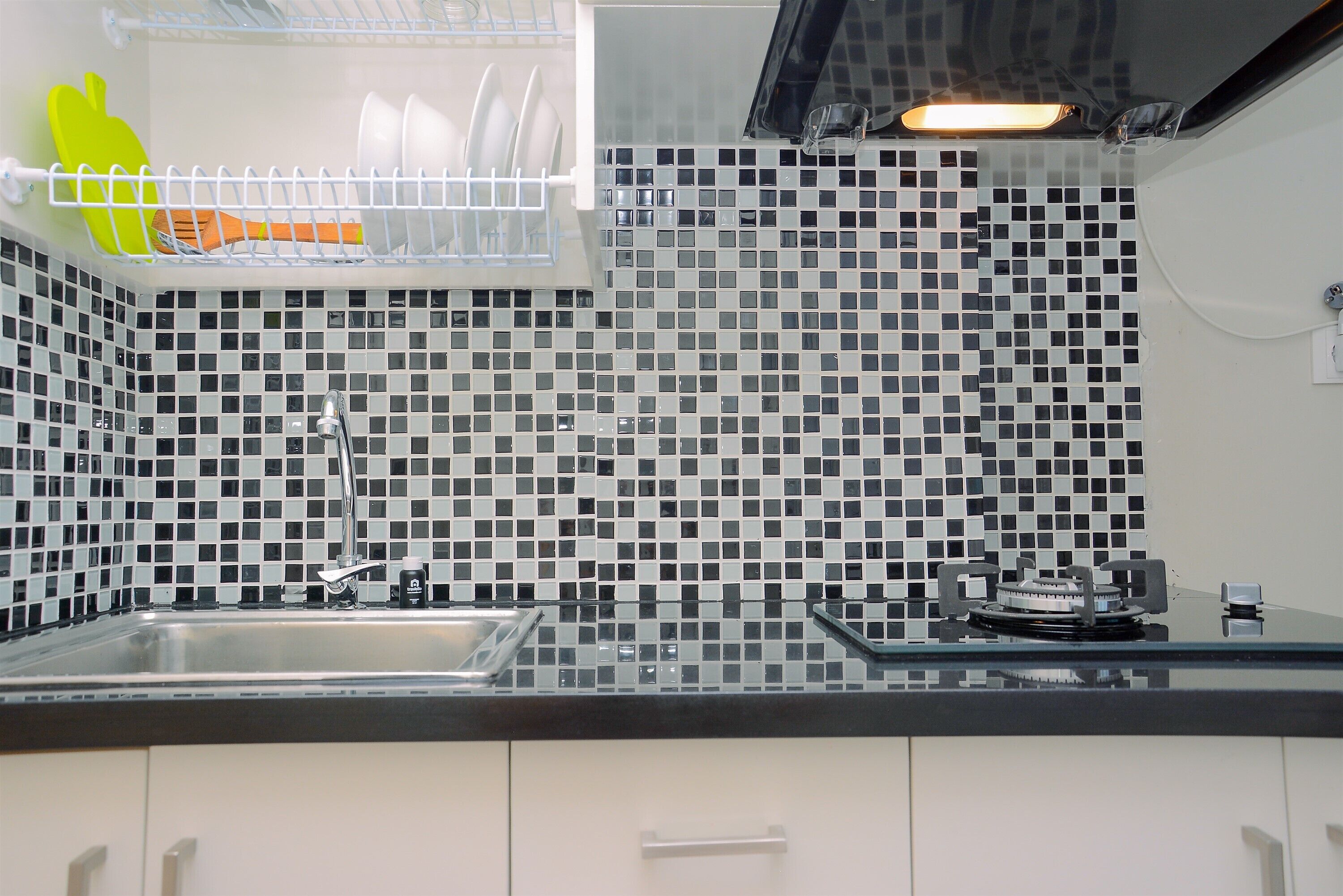 A kitchen with a black and white tiled backsplash, a stainless steel sink, and a gas stove.