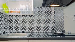 A kitchen with a black and white tiled backsplash, a stainless steel sink, and a gas stove. - Studio Apartment with Garden View at The Springlake View Summarecon (Bekasi)