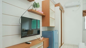 A compact room with a TV mounted on the wall, a wooden desk, a blue refrigerator, and a sliding door closet. - Homey Studio Margonda Residence 1 Apartment (Depok)