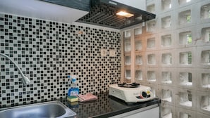 A kitchen with a black and white tiled backsplash, a stainless steel sink, a gas stove, and a ventilation hood. - Homey Studio Margonda Residence 1 Apartment (Depok)