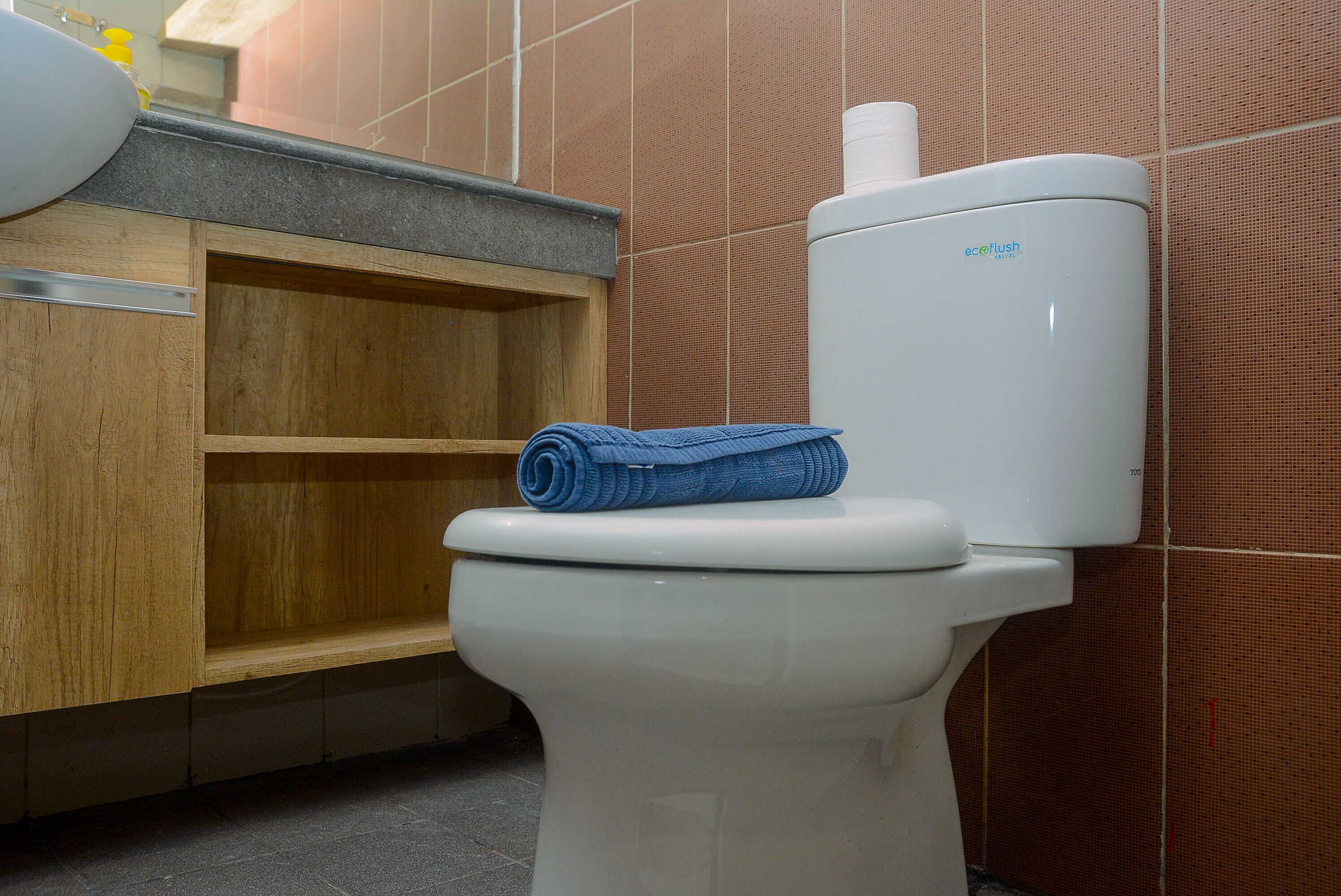 Inodoro con una toalla azul encima, un armario de madera debajo y tanque de inodoro blanco.