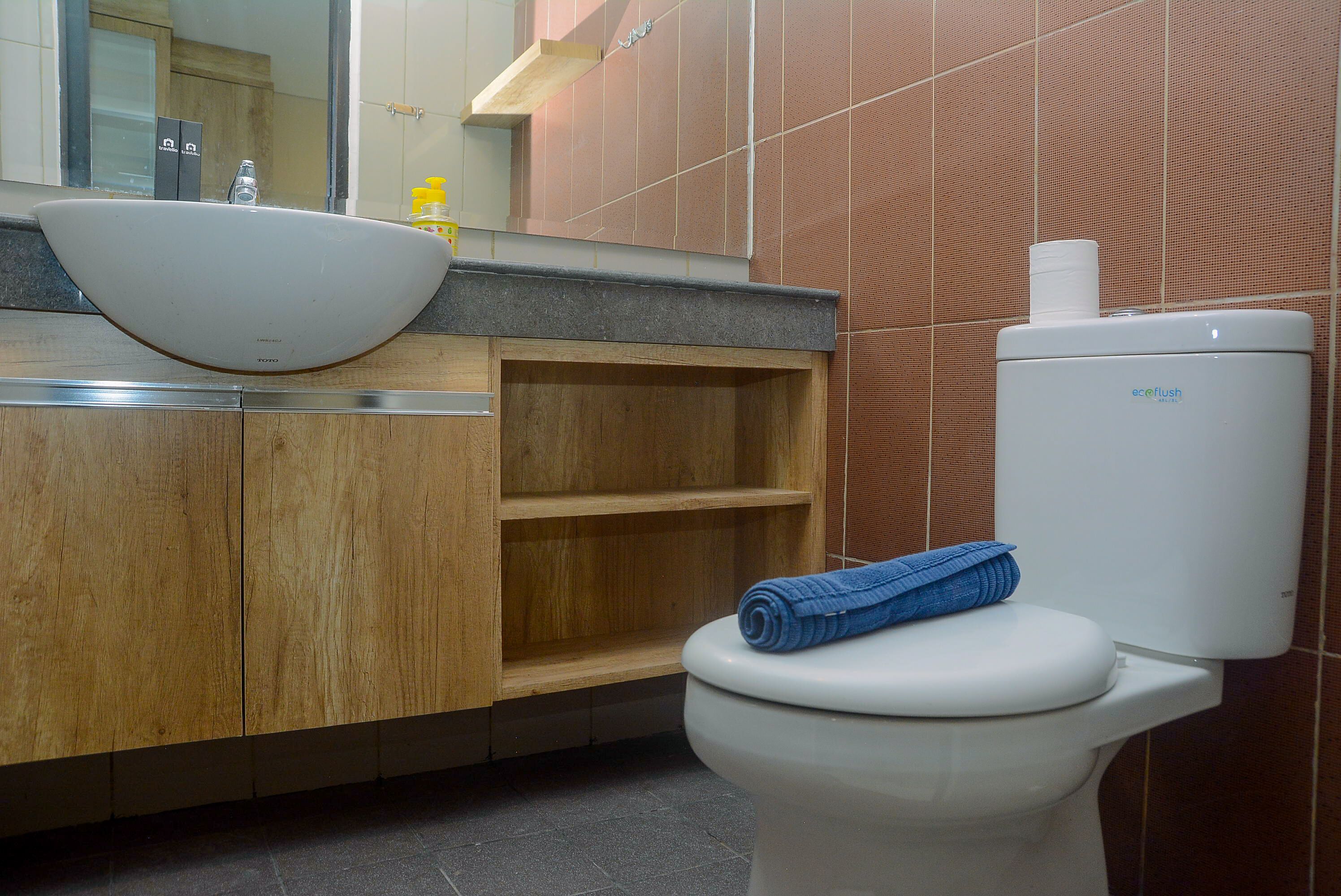 A bathroom with a white sink, wooden vanity, and a toilet with a blue towel on it.