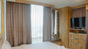 Une chambre d’hôtel avec un lit, une télévision, une armoire en bois et une fenêtre avec des rideaux.