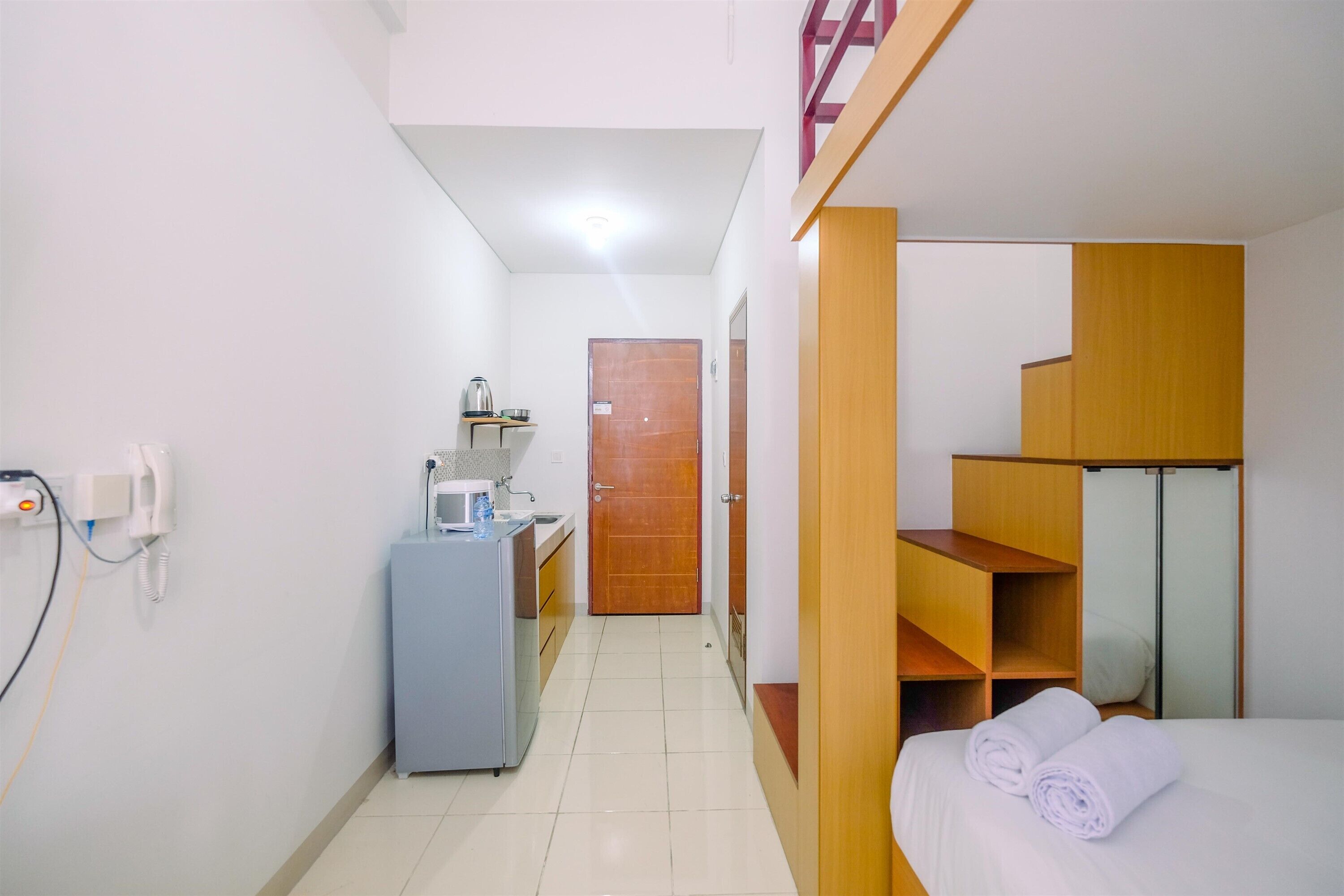 Quarto de hotel pequeno com cozinha compacta, uma cama e toalhas brancas bem dobradas, além de um guarda-roupa de madeira.