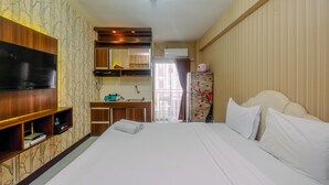 Habitación de hotel con una cama grande, televisión, escritorio con silla, armario y baño visible a través de una puerta de cristal.