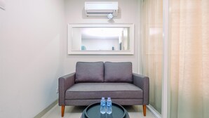 Una sala de estar moderna con un sofá gris, una mesita de centro redonda con dos botellas de agua, un espejo grande y un equipo de aire acondicionado en la pared.