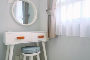 Une coiffeuse blanche avec un miroir rond, deux tiroirs et un tabouret doté d’un coussin en denim.