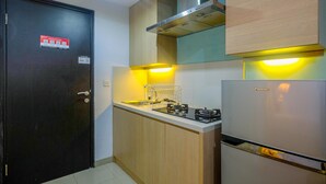 A compact kitchen with a black door, a built-in stove, and a refrigerator. - Warm and Cozy Studio Park View Condominium Apartment (Depok)