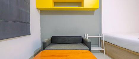 Una habitación pequeña con sofá, una mesita, una cama y un estante amarillo.