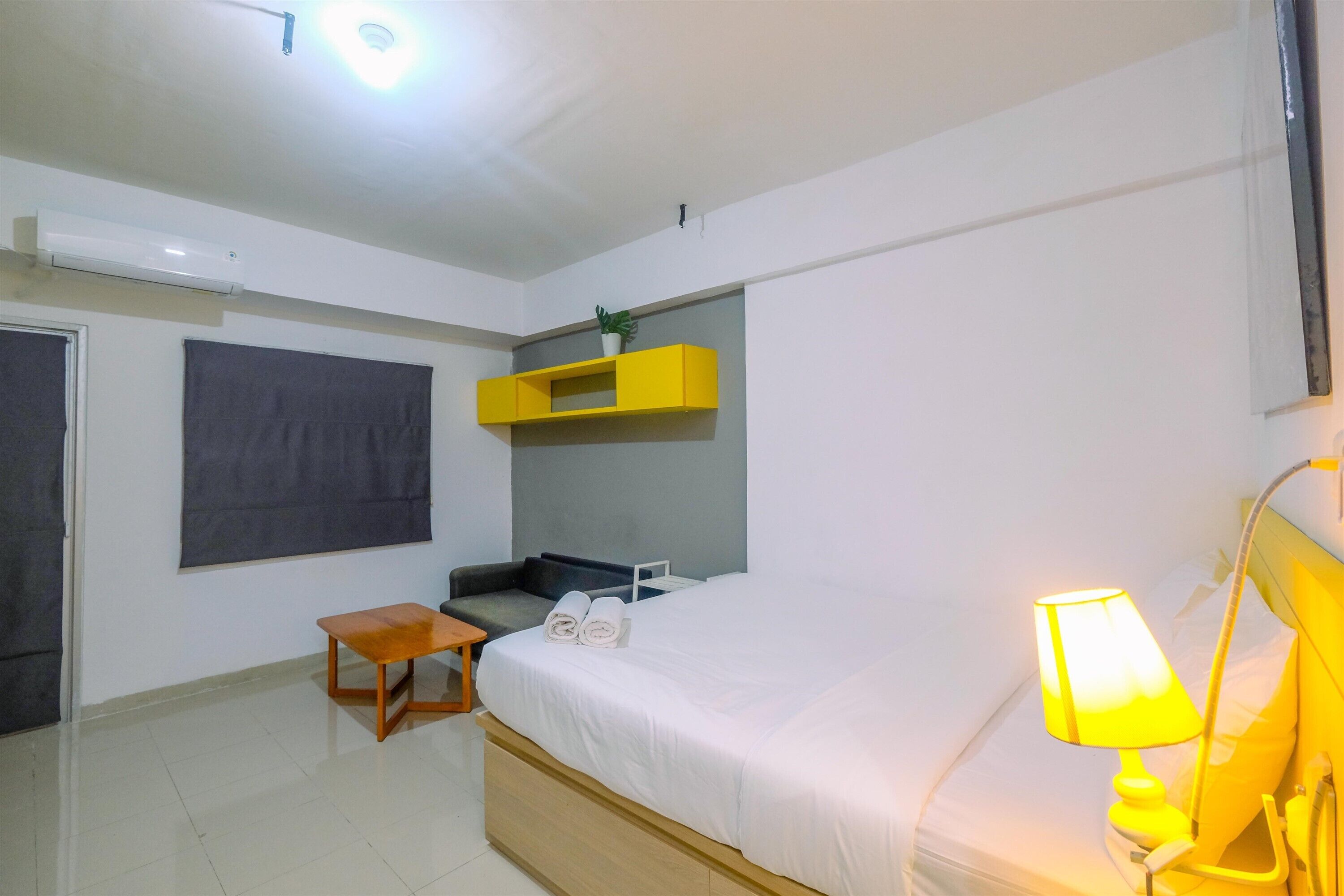 Une chambre d’hôtel avec un lit, une petite table, une chaise, une étagère et une lampe.