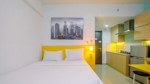 A hotel room with a bed, a cityscape painting, a yellow wall, a kitchen area with a stove, and a sink. - Warm and Cozy Studio Park View Condominium Apartment (Depok)