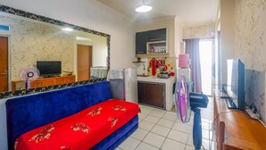 A compact living space with a blue sofa, a small kitchenette, a television, and a fan.