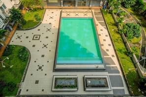 Vista aérea de una piscina rodeada por una terraza con baldosas de diseño geométrico, bordeada de vegetación y un muro bajo.