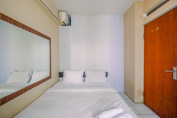Quarto de hotel com uma cama grande, uma porta de madeira e um ar condicionado fixado na parede.