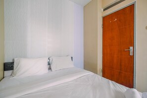 Habitación de hotel con cama, dos almohadas, una puerta de madera y pared con textura.