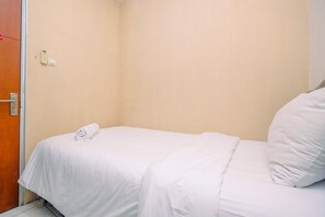 Uma cama pequena e bem arrumada, com lençol branco e toalha enrolada.