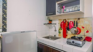 A kitchen with a refrigerator, a sink, a stove, and various utensils hanging on the wall.