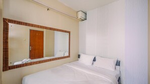 A hotel room with a large bed, a mirror, a door, and an air conditioning unit.